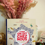 Première de couverture de l'ouvrage Comme on dit chez nous, mis en scène debout devant un bouquet de fleurs séchées roses